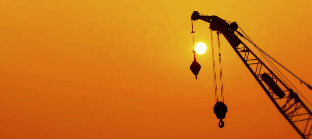 istock Hoisting cranes working on beautiful cloudy sky with orange sunset and rays of light background. 1201494519