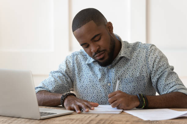 istock Focused african American male studying at laptop making notes 1201494931