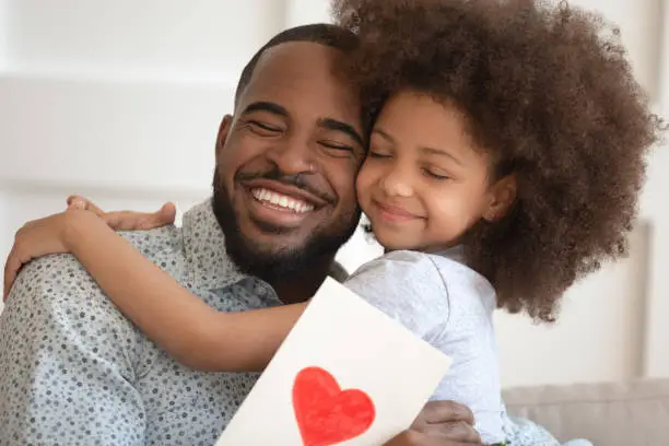 Photo of Cute little biracial daughter greeting dad with postcard