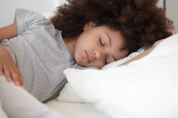 calm little biracial girl sleeping peacefully in white bed - sleeping child bedtime little girls imagens e fotografias de stock