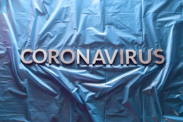 the word coronavirus laid with silver letters on crumpled blue plastic film - centered flat lay composition with dramatic light