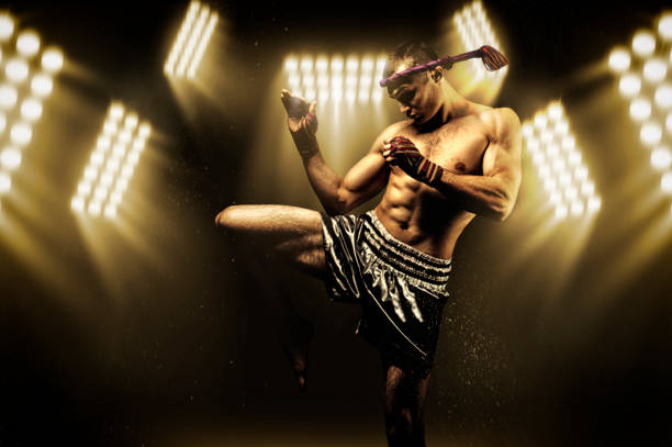 サーチライトに囲まれたリングのキックボクサーは、戦いの前に伸びる。彼の膝でスイングの動きを行います。モンクホン - muay thai ストックフォトと画像