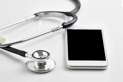 Shot of a stethoscope lying on top of a mobile phone against a white background