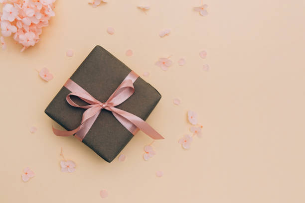 istock Gift box wrapped in craft paper with pink ribbon on pale orange background with hydrangea flowers. 1201505364