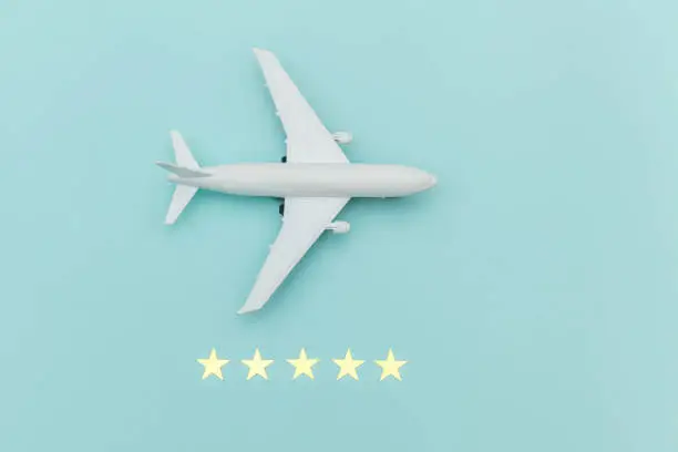 Photo of Simply flat lay design miniature toy model plane and 5 stars rating on blue pastel colorful trendy background. Travel by plane vacation summer weekend sea adventure trip journey ticket tour concept