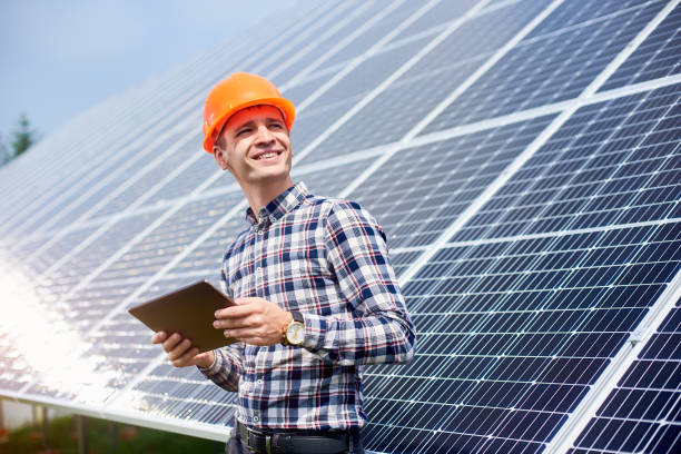 hombre sonriente con tableta en las manos cerca de la estación solar. generación de energía ecológica verde. - solar panel engineer solar power station solar energy fotografías e imágenes de stock