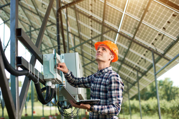 operador en casco y con portátil en la estación comprobando el funcionamiento de la planta de energía solar. - solar panel engineer solar power station solar energy fotografías e imágenes de stock