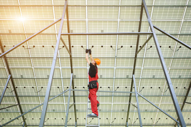 istock Installing and wiring of solar photo voltaic panel. Worker in orange uniform connects solar panels at the station. 1201506601