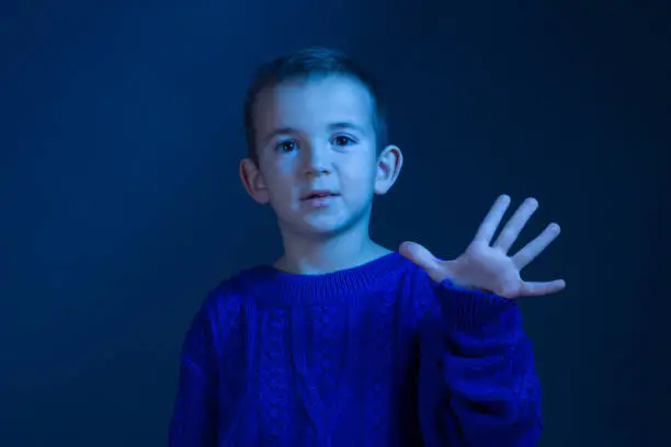 Photo of Studio portrait of a brunette Boy who counts on his fingers, shows five fivefinger