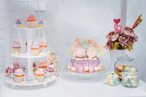 Candy bar with birthday cake, cup cakes and meringue on a light background. Yellow, purple, blue, pink colors.
