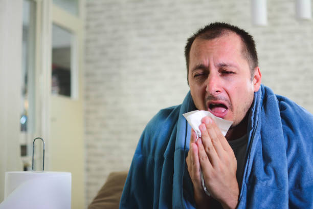 istock Man sneezing in a tissue in the living room 1201510567