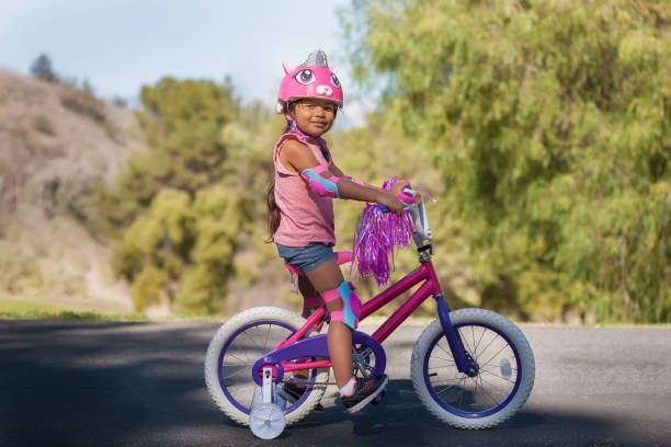mädchen mit rosa fahrrad und sicherheitsausrüstung, lernen, ein fahrrad mit trainingsrädern zu fahren. - stützrad stock-fotos und bilder
