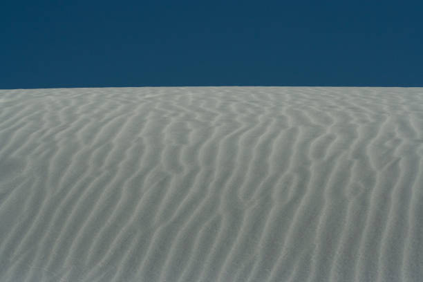 Fermez-vous vers le haut de la dune blanche avec des modèles d'onde et le ciel bleu clair au monument national de sables blancs - Photo