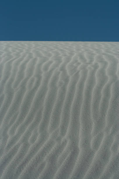 Fermez-vous vers le haut de la dune blanche avec des modèles d'onde et le ciel bleu clair au monument national de sables blancs - Photo