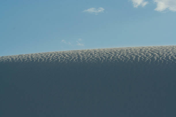 Fermez-vous vers le haut de la dune blanche avec des modèles d'onde et le ciel bleu clair au monument national de sables blancs - Photo