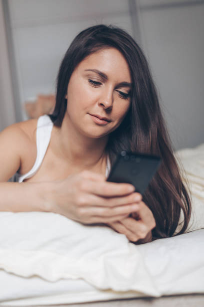 istock Young woman with smartphone texting message in bed at home 1201515641