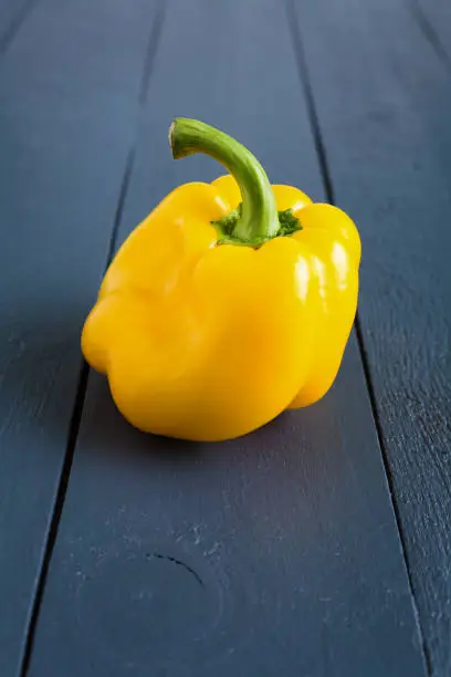 One ugly, deformed shaped yellow bell pepper on the wooden gray background close up. Imperfect, strange organic vegetable. Misshapen produce, food waste problem concept. Vertical orientation composition.