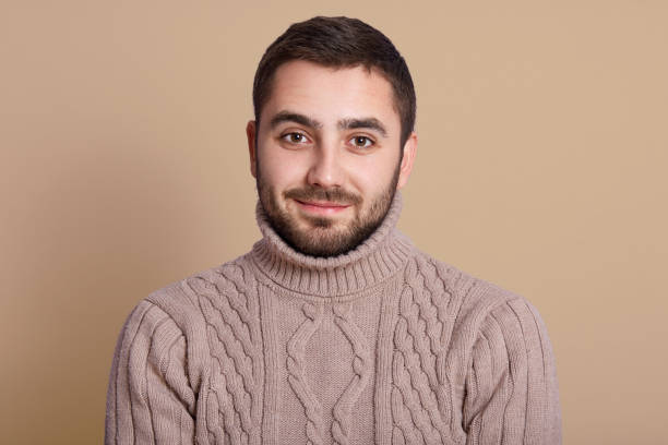 istock Studio shot of bearded man with pleasant appearance, looking directly at camera, posing isolated over beige background, handsome male wearing warm knitted sweater, being in good spirit, looks calm. 1201517419