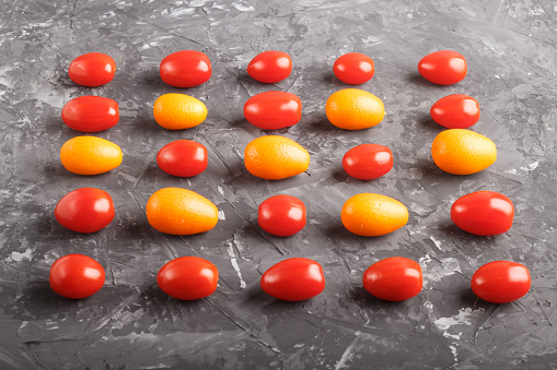 Rows of cherry tomatoes and kumquats on a black concrete background, side view, contrast concept.