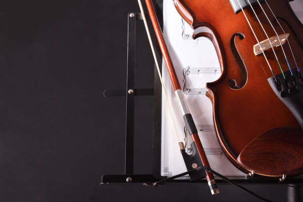 istock Violin closeup with bow music stand and score black background 1201518601