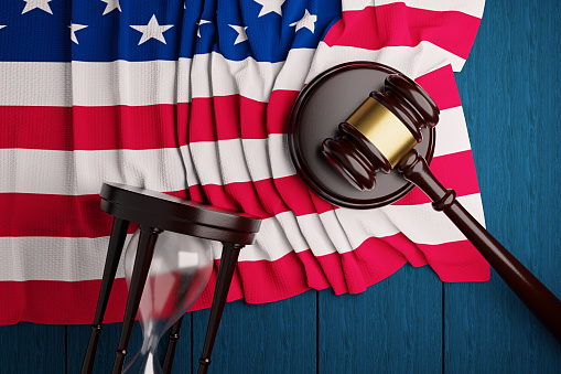 The judge's hammer,the US flag, and an hourglass lie on a blue wooden table.3D rendering.