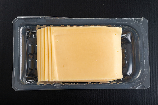 Slices of yellow cheese in a plastic package. Food from the market on the kitchen table. Dark background.