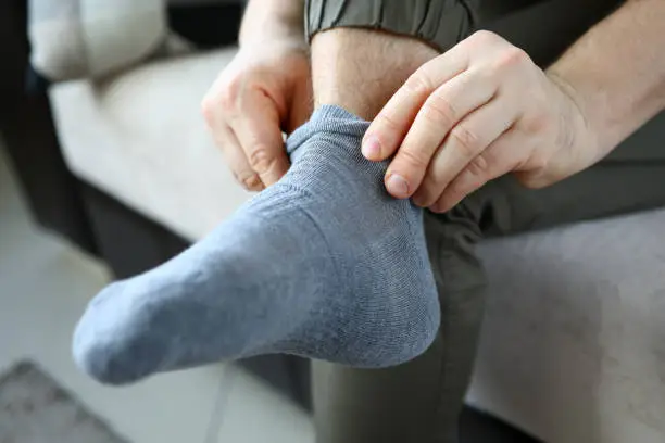 Man at home in morning puts gray socks on his leg. For a long time do not change clothes concept