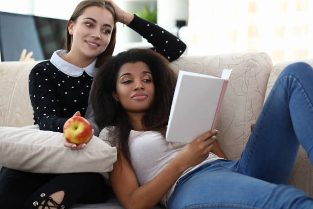 two woman frend read book sit on coach against - frend imagens e fotografias de stock