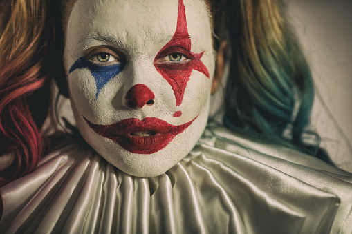 Young woman dressed as scary Joker. She is serious, but her make-up makes her face looks like smiling.