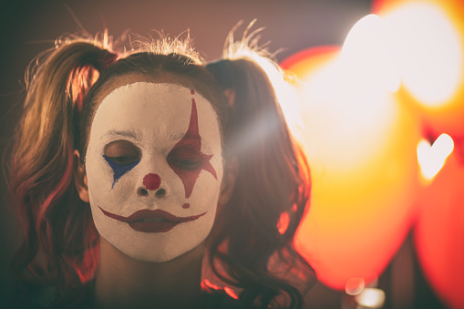 Young woman dressed as scary Joker. She is serious, but her make-up makes her face looks like smiling.