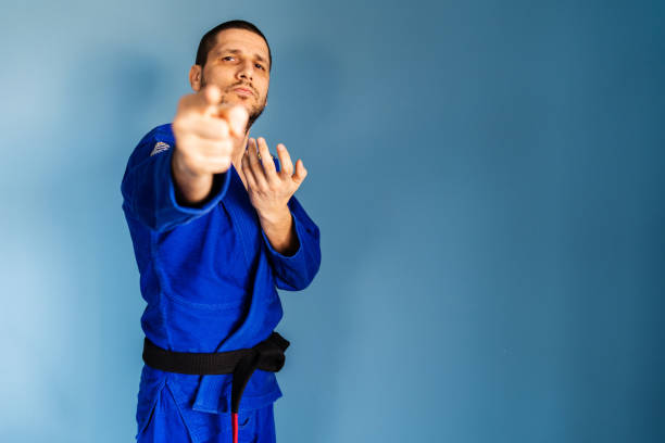 brasilianische jiu jitsu bjj kaukasischen athleten lehrer professor oder kämpfer vor der blauen wand stehend mit kimono gi einheitliche frontansicht zeigt finger zur kamera - ju jitsu stock-fotos und bilder
