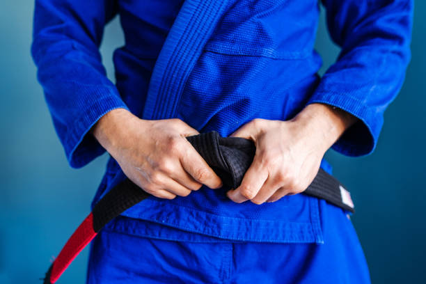 Close up on midsection of the bjj brazilian jiu jitsu black belt hands holding tied around the waist of an athlete fighter wearing blue kimono gi standing in front of the wall Close up on midsection of the bjj brazilian jiu jitsu black belt hands holding tied around the waist of an athlete fighter wearing blue kimono gi standing in front of the wall brazilian jiu jitsu photos stock pictures, royalty-free photos & images