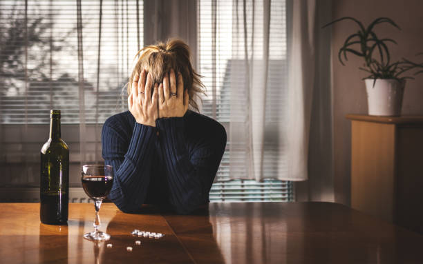 Depressed woman is drinking red wine and taking pills at home alone Head in hands. Alcohol and drug addiction concept. Social issues alcohol abuse stock pictures, royalty-free photos & images