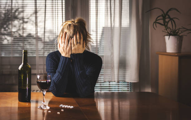 mulher deprimida está bebendo vinho tinto e tomando pílulas em casa sozinha - abuso de álcool - fotografias e filmes do acervo