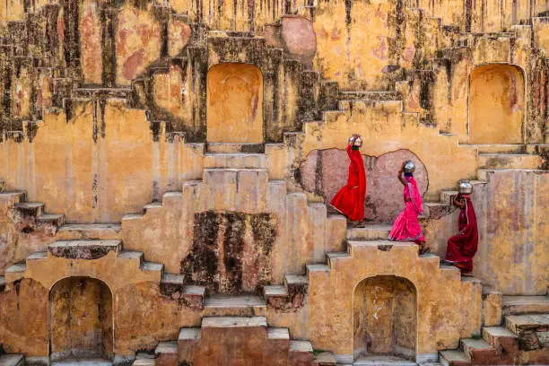 Indian women carrying water from stepwell near Jaipur, Rajasthan, India. Women and children often walk long distances to bring back jugs of water that they carry on their head. 
Stepwells are wells in which the water may be reached by descending a set of steps.