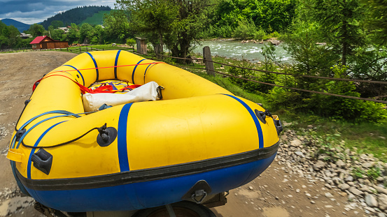 Big yellow rubber boat on the mountain road by riverside. Close-up photo. Rafting on mountain rivers. Extreme and activity concept.