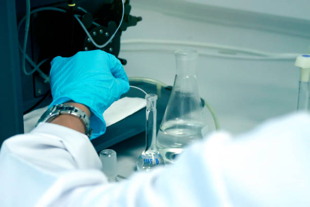 Research scientist hand with blue chemical protective gloves using volumetric flask for doing experiment to determine the levels of heavy metals in solutions by ICP (Inductively Coupled Plasma spectrometer). Chemist working in chemistry laboratory with instrument concept. científico investigador mano con guantes de protección química azul utilizando matraz volumétrico para hacer experimento para determinar los niveles de metales pesados en soluciones por icp (espectrómetro de plasma acoplado inductivamente). químico q