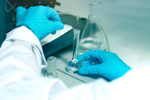 Research scientist hand with blue chemical protective gloves using volumetric flask for doing experiment to determine the levels of heavy metals in solutions by ICP (Inductively Coupled Plasma spectrometer). Chemist working in chemistry laboratory with instrument concept.