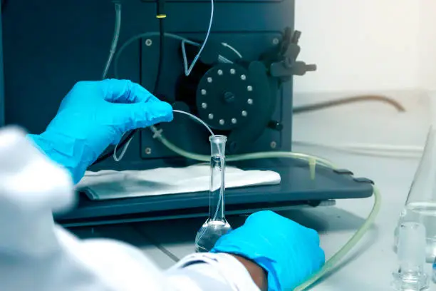 Research scientist hand with blue chemical protective gloves using volumetric flask for doing experiment to determine the levels of heavy metals in solutions by ICP (Inductively Coupled Plasma spectrometer). Chemist working in chemistry laboratory with instrument concept.