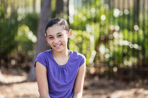 An Hispanic girl, 10 years old, hanging out at a park, on the playground, on a sunny spring or summer day.  She is smiling at the camera.