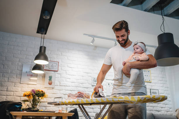 istock Hard-working single father ironing clothes while holding his baby daughter 1201538771