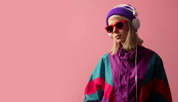 Beautiful blonde woman in 90s clothes with sunglasses and headphones on pink background