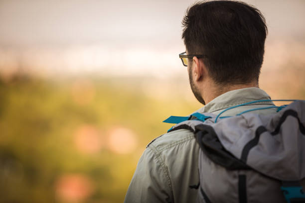 Close up of head and shoulders rear view of a man wearing a backpack and looking towards the horizon.