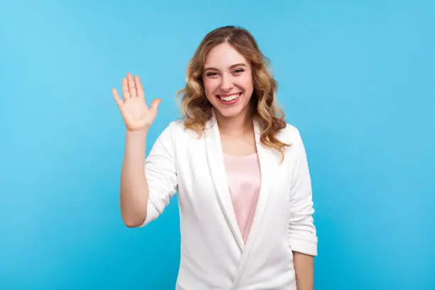 Photo of Hello! Portrait of friendly kind cheerful girl waving hand saying hi welcome, smiling. isolated on blue background