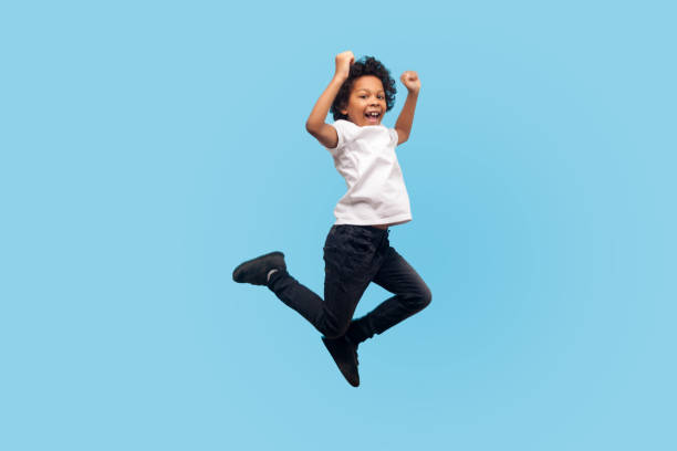 full length, lively energetic little boy in t-shirt and denim jumping in air screaming with happiness - youth and age imagens e fotografias de stock