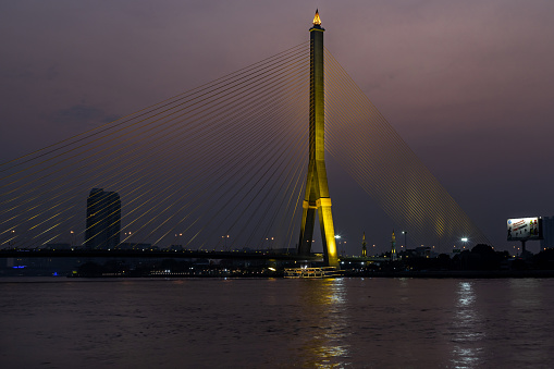 Bangkok, thailand 21 Jul, 2019 : Rama VIII bridge, Rope Bridge across the Chao Phraya River, A tall V-shape pylon tower with view blue sky is background and Cityscape at night of Bangkok.