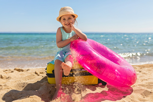 Beautiful smiling child at a beach with a inflatable ring, and a suitcase,