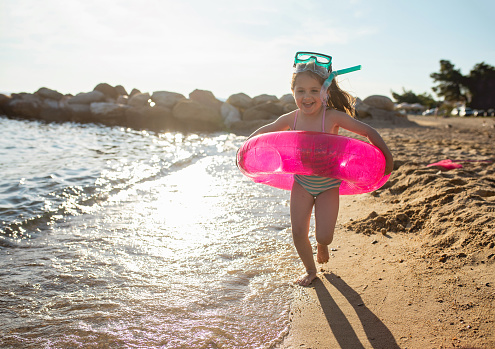 Beautiful playful child running on a beach with an inflatable ring and skuba mask.