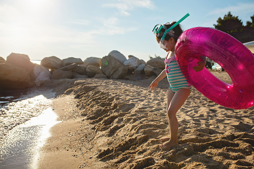 Beautiful playful child on a beach with an inflatable ring and skuba mask.