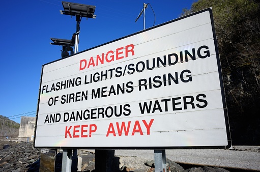 Close up of sign that reads danger flashing lights sounding of siren means rising and dangerous waters keep away